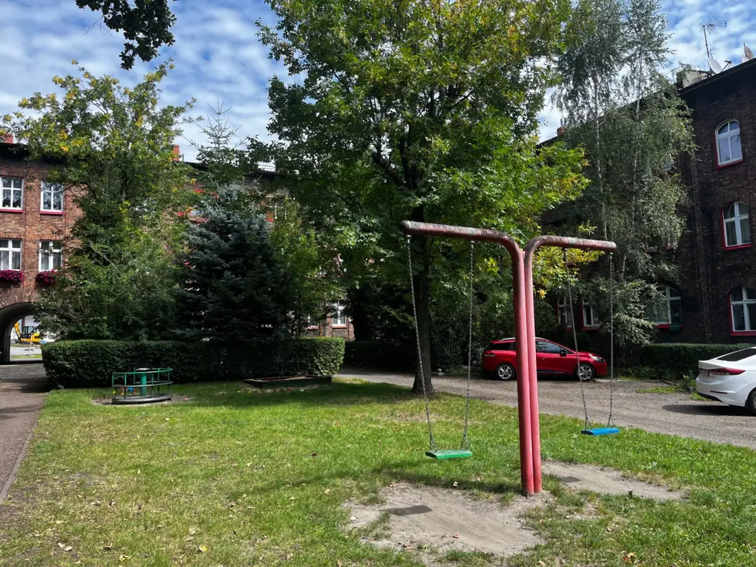 Podwórze w Nikiszowcu: trawnik z huśtawką między ceglanymi budynkami osiedla.