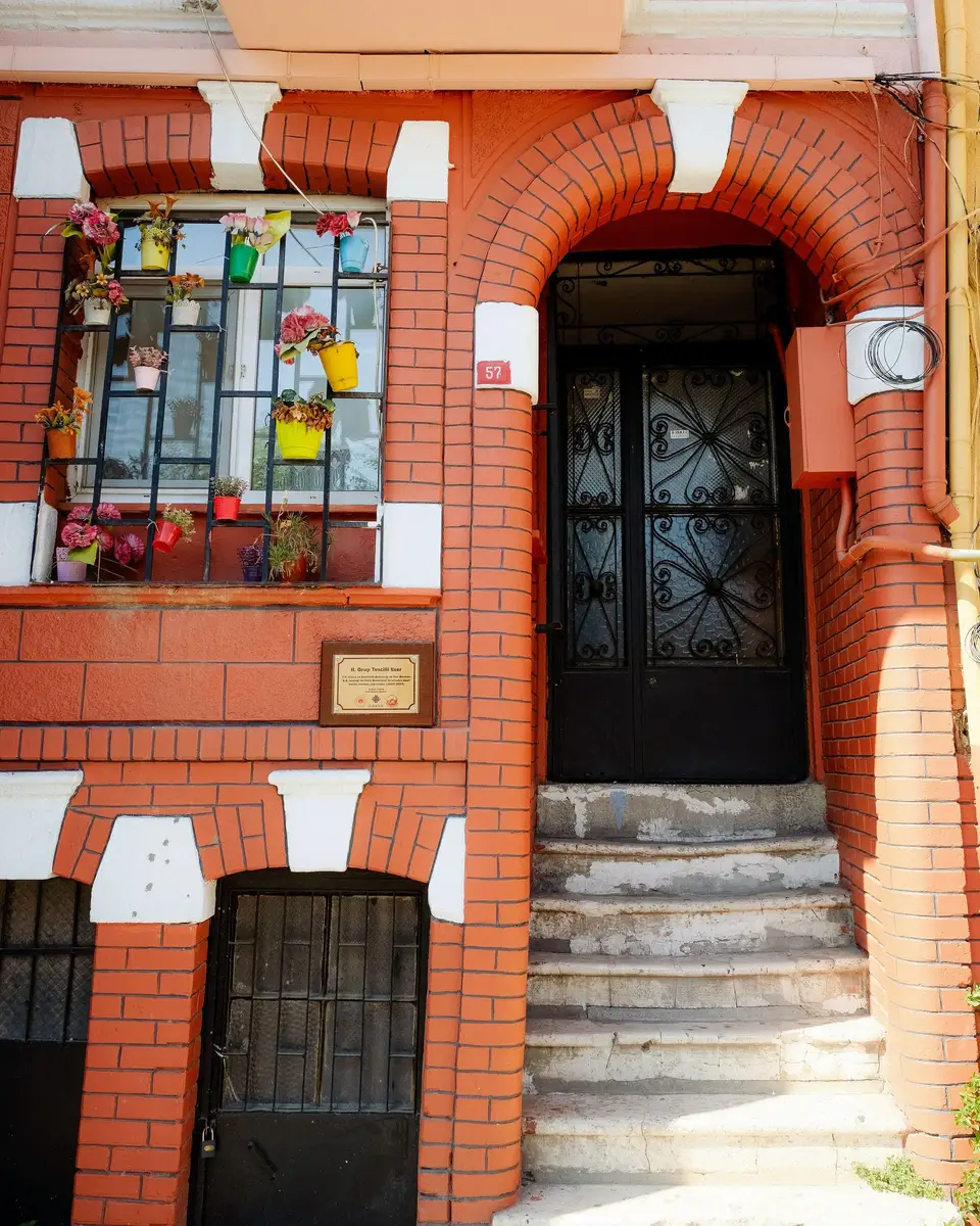 Ceglana elewacja z łukowym wejściem, kamiennymi schodami i witrażowym oknem obok drzwi.